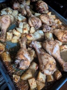Chicken drumsticks seasoned with za'atar, herbs, and spices are baked in a pan alongside cubed potatoes. The dish appears browned, juicy, and freshly cooked, with visible seasoning on both the za'atar chicken and potatoes.