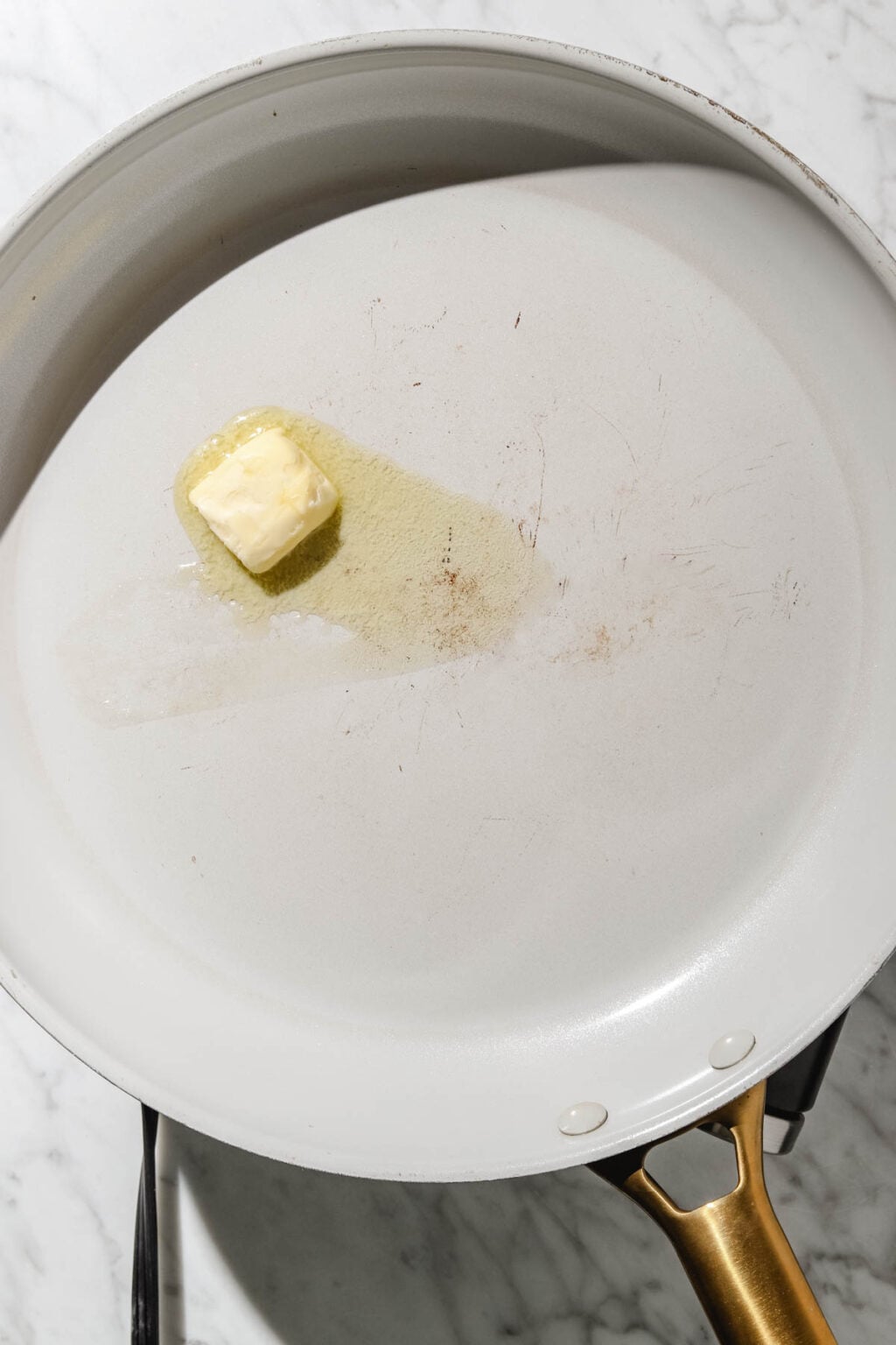 large light grey skillet with knob of butter melting on a light marble background