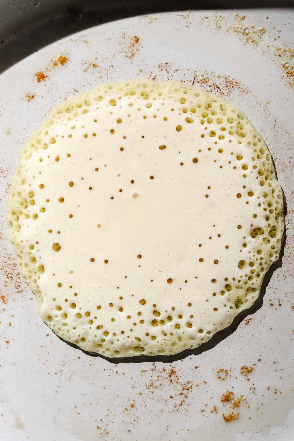 Baghrir cooking in skillet, pancake with bubbles in a light grey buttered skillet