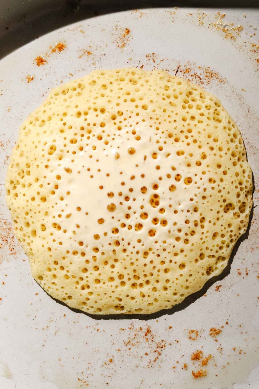 Baghrir cooking in skillet, pancake with bubbles in a light grey buttered skillet
