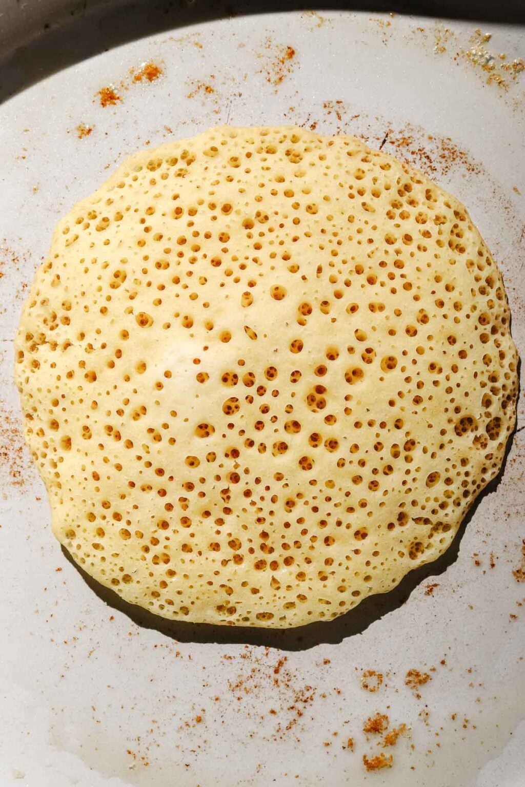 Baghrir cooked in skillet, pancake with bubbles in a light grey buttered skillet