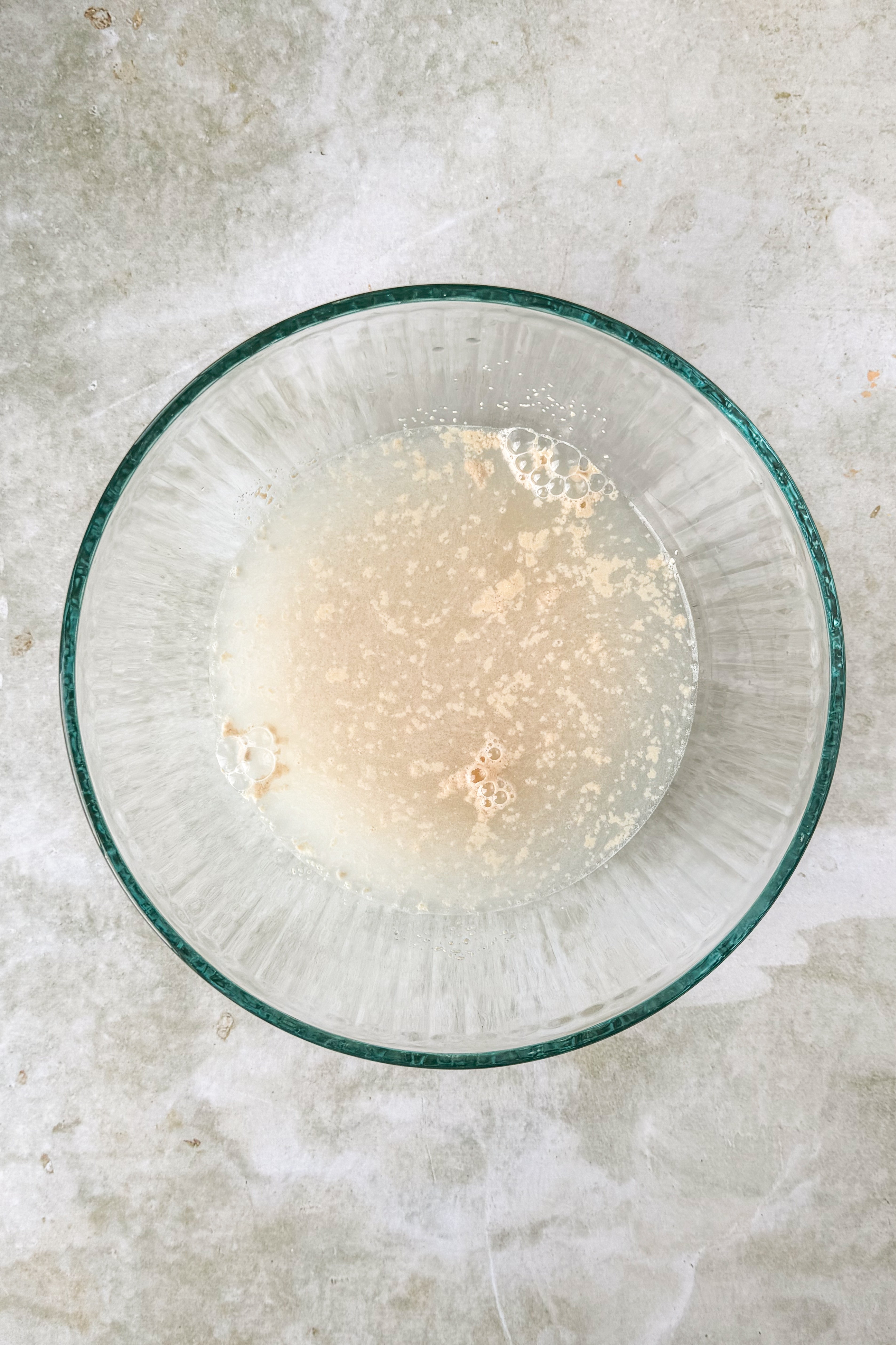 Glass bowl with water and yeast on an olive green marble background.