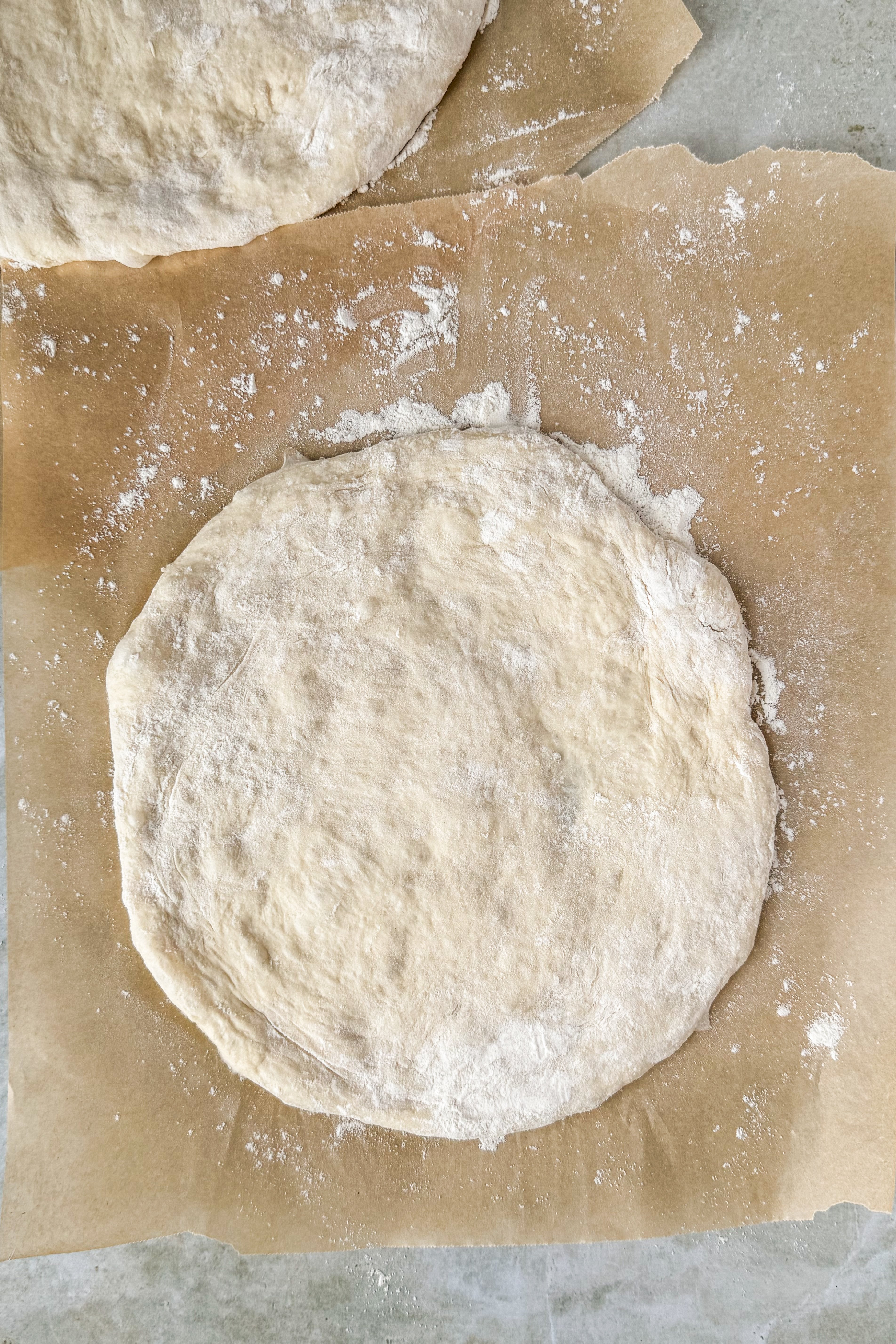 Two dough circles on floured parchment paper on an olive marble background.