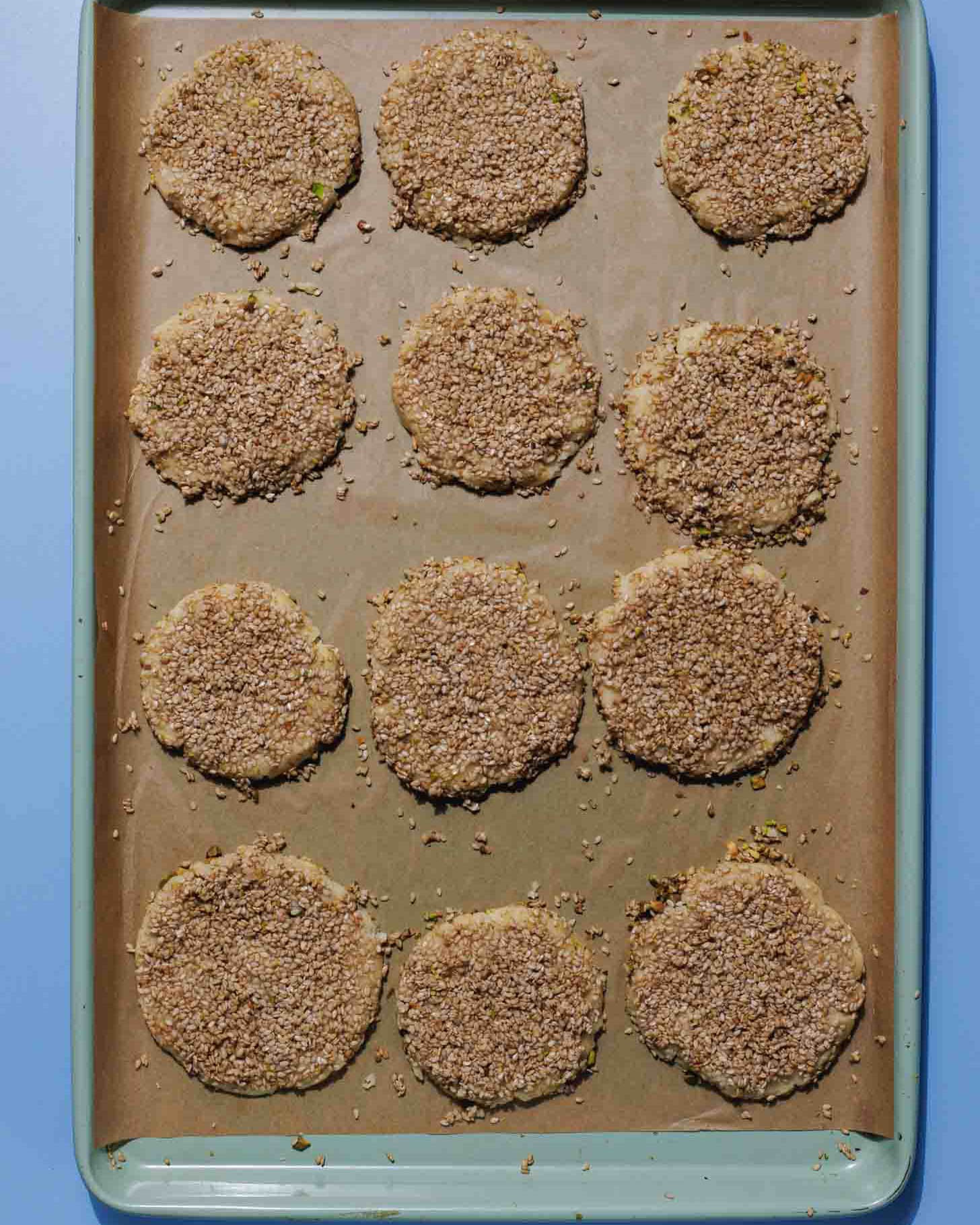 Twelve round, crumb-coated cookies are evenly spaced on a parchment-lined baking sheet with a blue edge, ready to be baked.