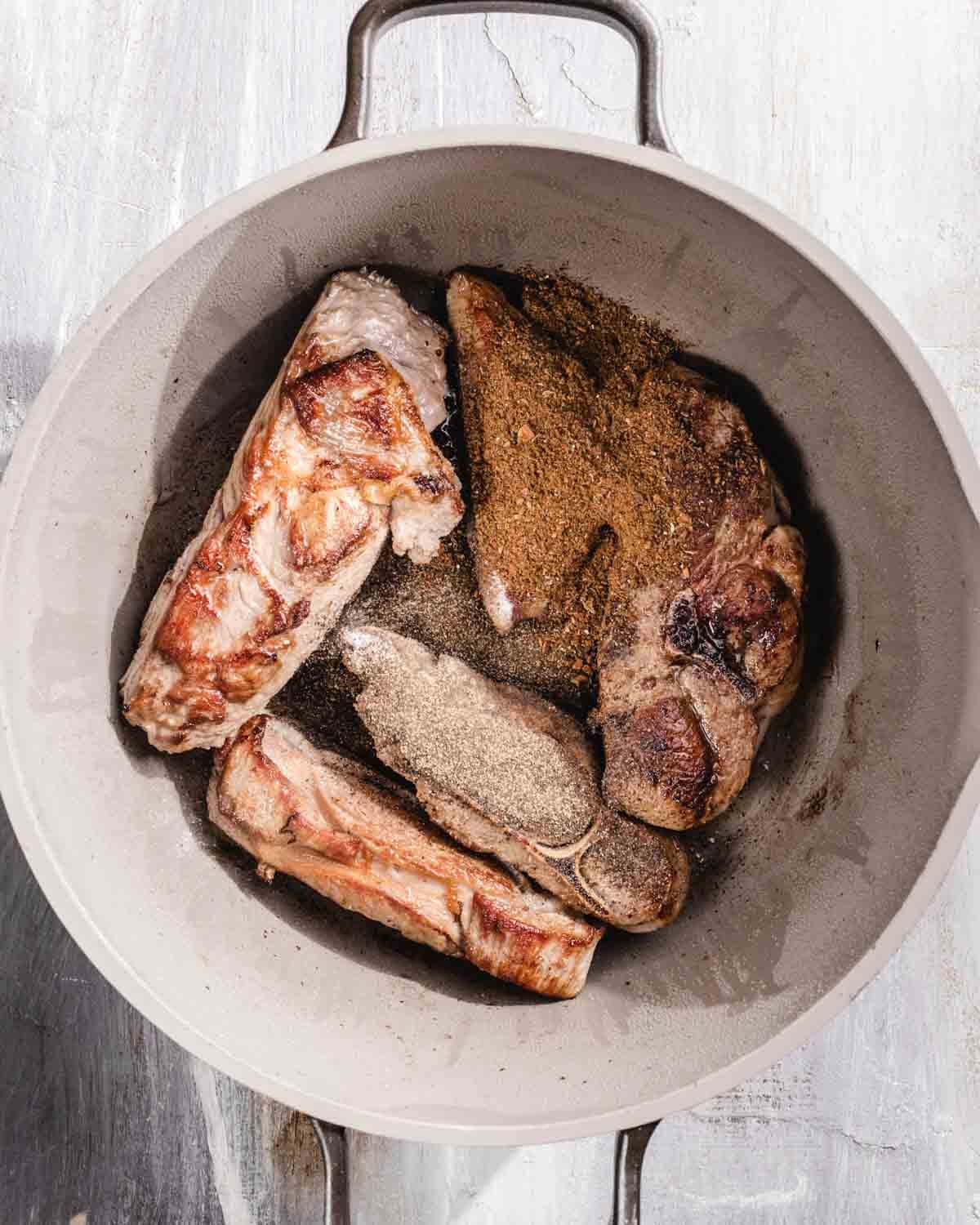 A white pot containing browned pieces of meat seasoned with a generous amount of ground spices on top, seen from above.
