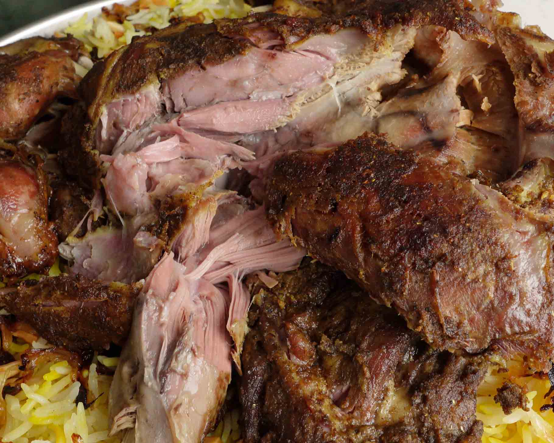 Close-up of tender, roasted lamb pieces served on a bed of yellow rice, showing juicy, shredded meat with a browned, seasoned crust.