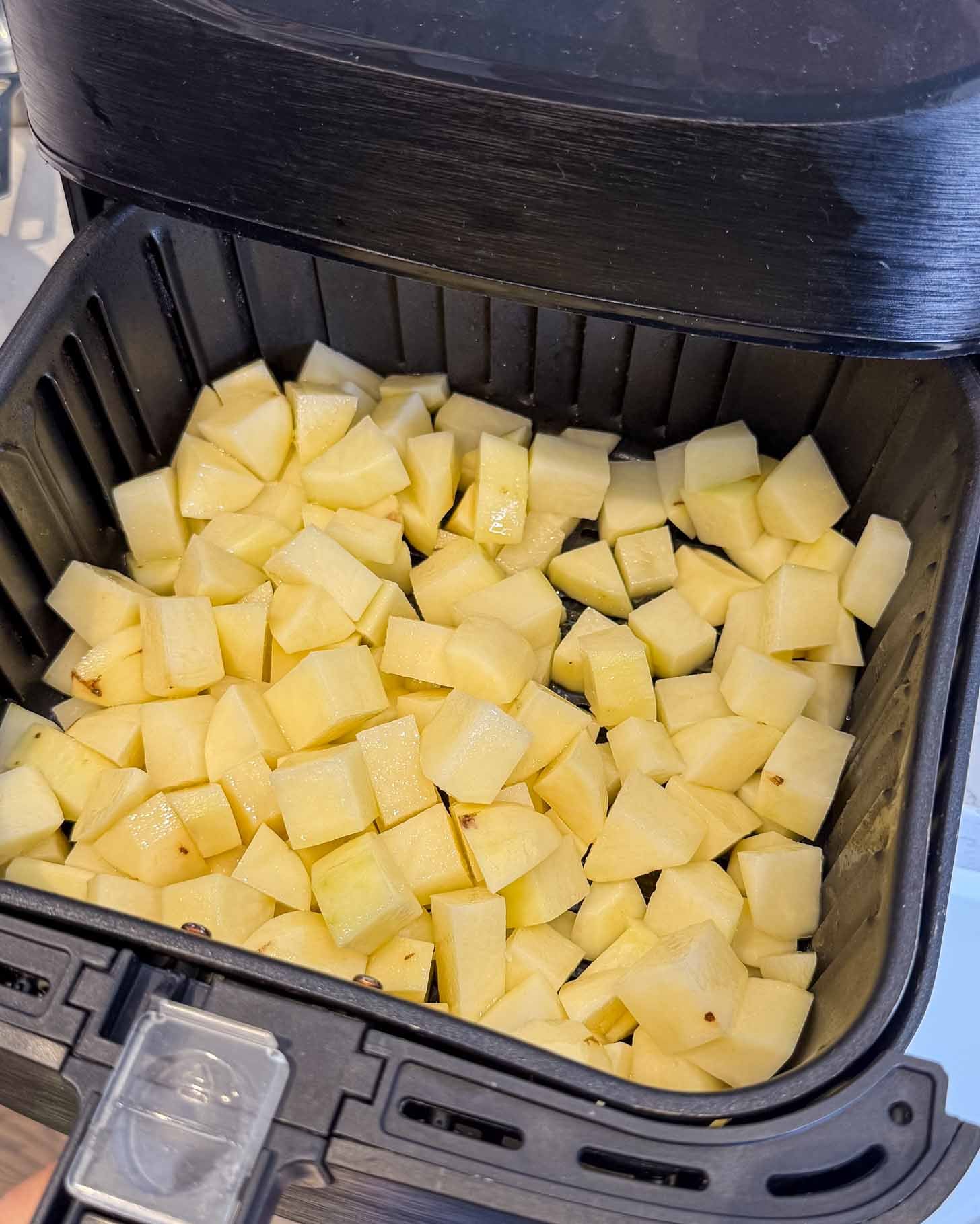 Diced potatoes are spread in a single layer inside an air fryer basket, ready to be cooked.