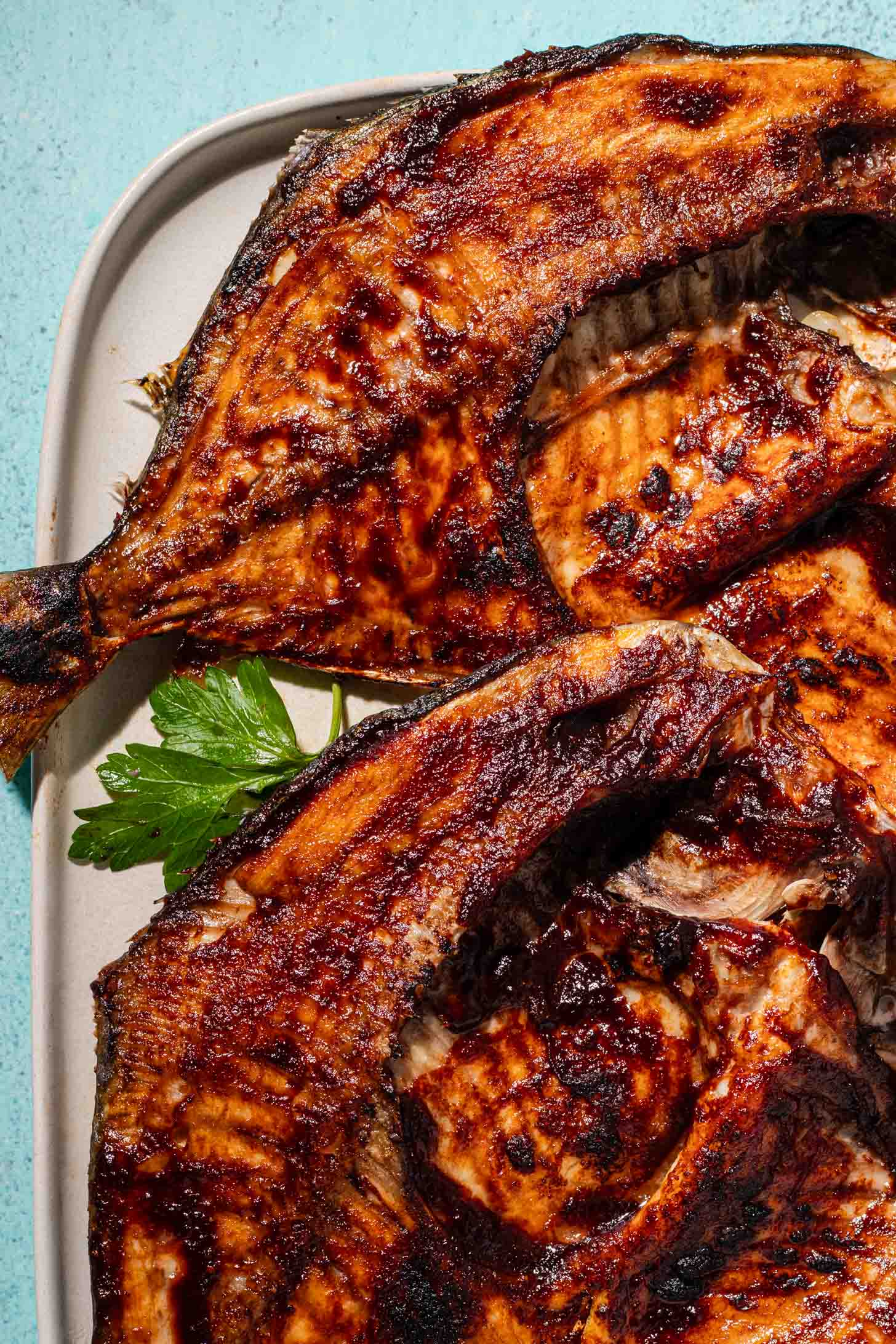 Grilled fish with crispy, golden-brown skin on a white plate, garnished with fresh parsley.
