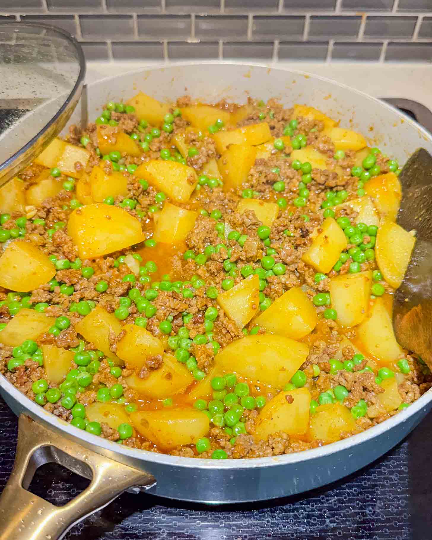 A skillet filled with cooked ground meat, diced potatoes, and green peas in a savory sauce sits on a stovetop, ready to serve.