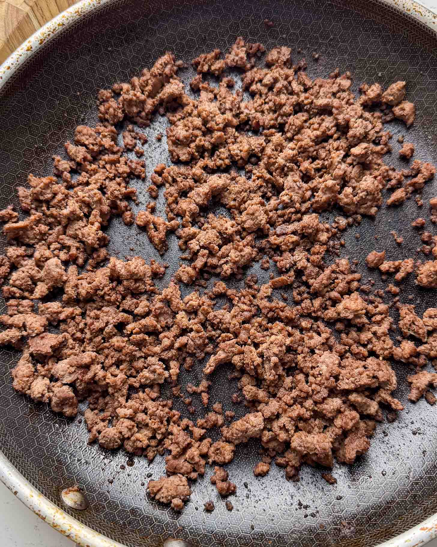 Cooked ground beef scattered in a nonstick frying pan, with a honeycomb-textured surface visible underneath the browned meat.