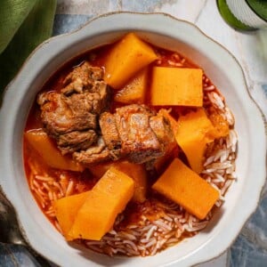 A bowl of stew featuring braised pork ribs and chunks of squash served over white rice.
