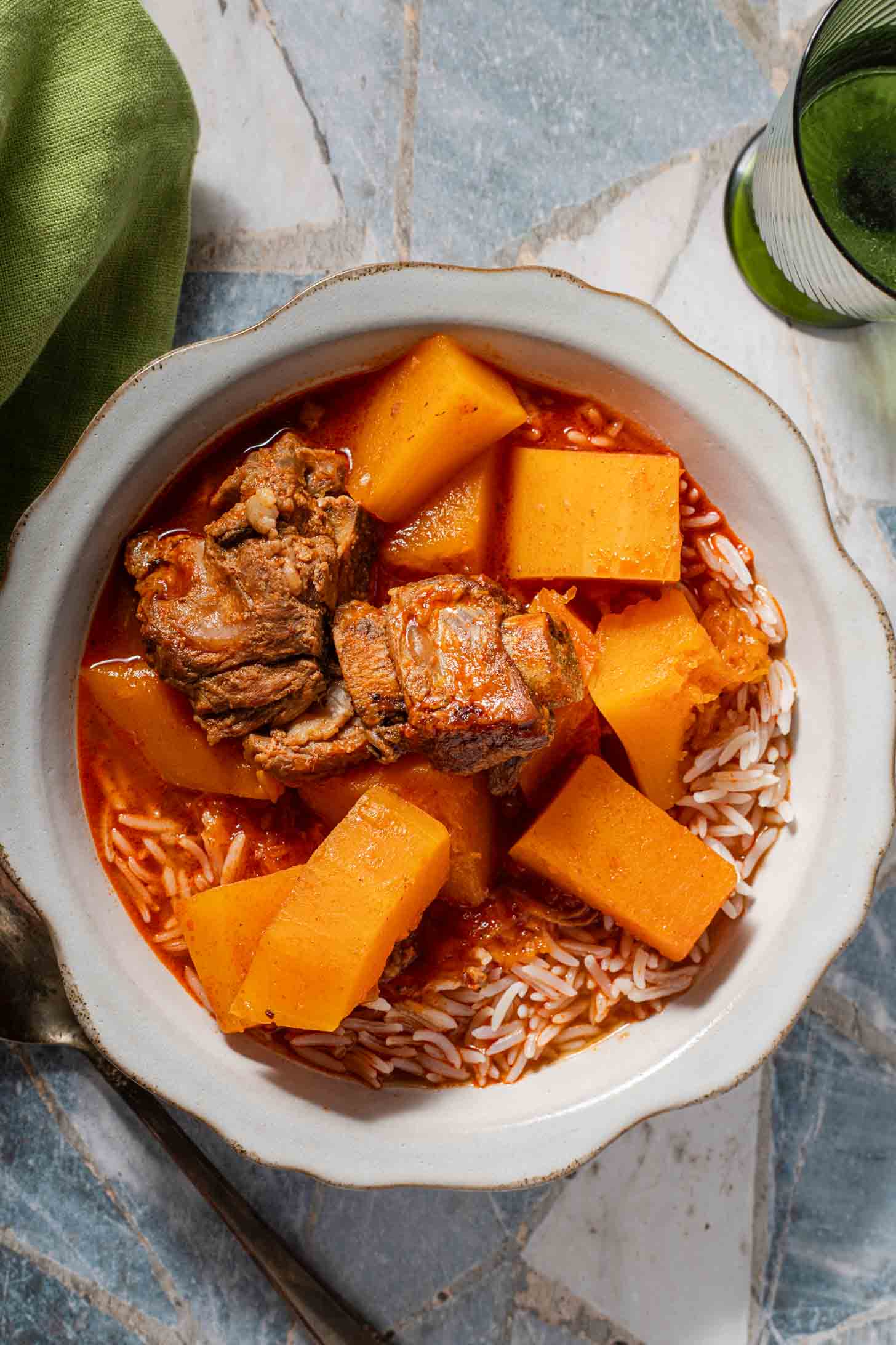 A bowl of stew featuring braised pork ribs and chunks of squash served over white rice.