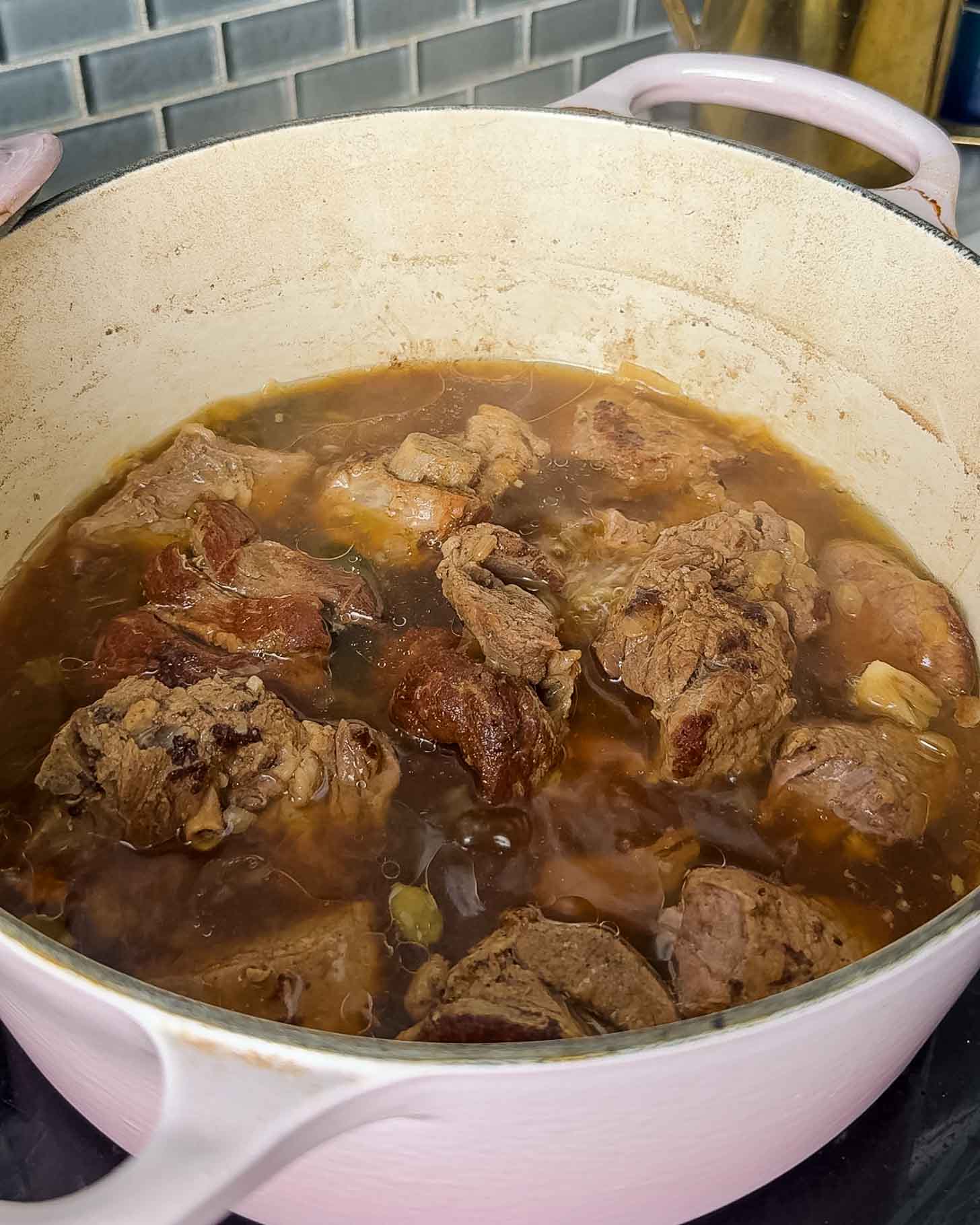 Chunks of browned meat simmering in a broth inside a light-colored enameled cast iron pot.