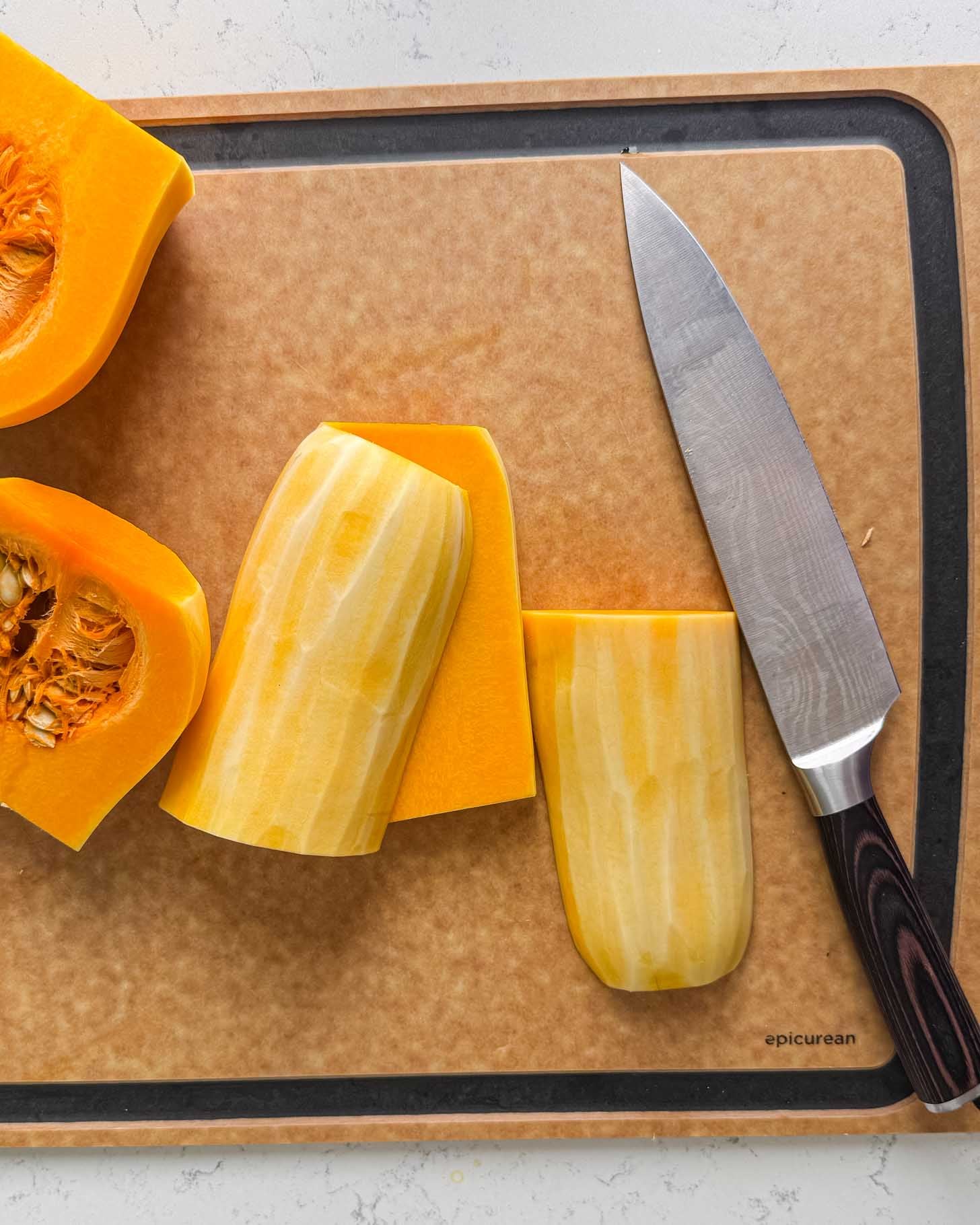 A chefs knife and cut pieces of peeled butternut squash on a cutting board.