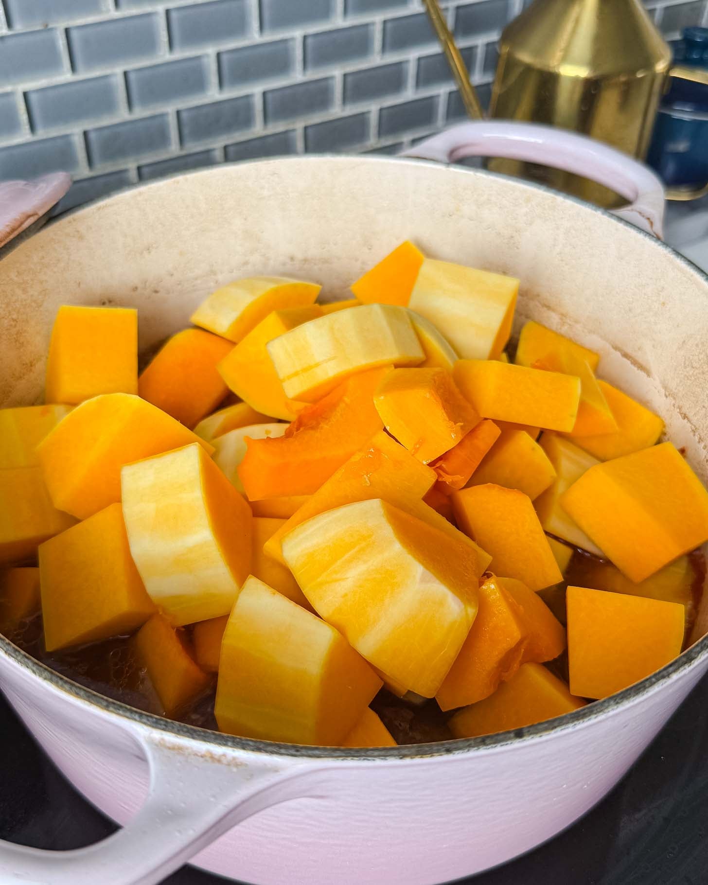 Chunks of raw, orange squash in a light pink enameled Dutch oven.