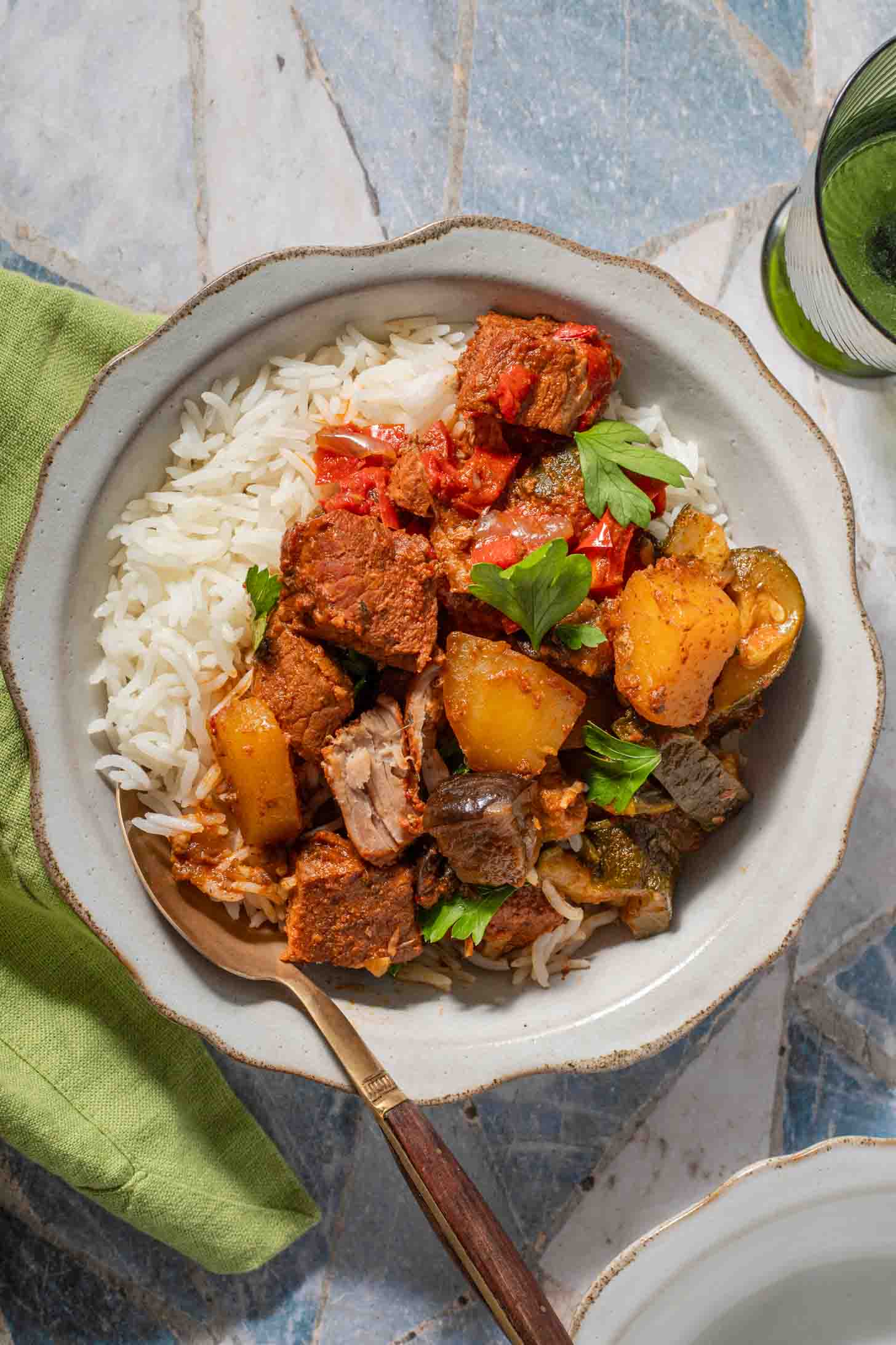 A bowl of beef and potato stew served over white rice, garnished with fresh parsley.
